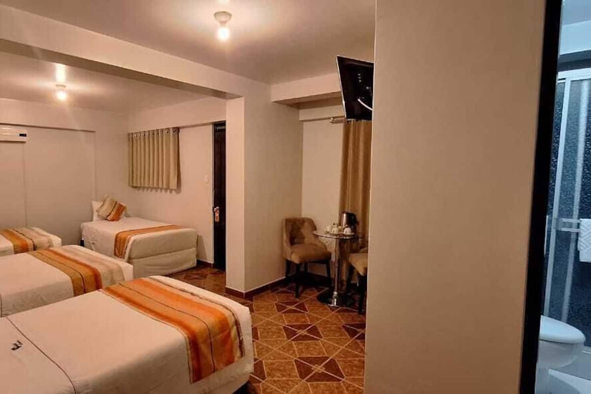 A hotel room with two beds, a small table with a chair, a TV, and a window with a curtain.