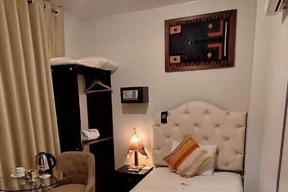 A neatly arranged bedroom with a bed, a bedside table, a lamp, a chair, and a wardrobe.