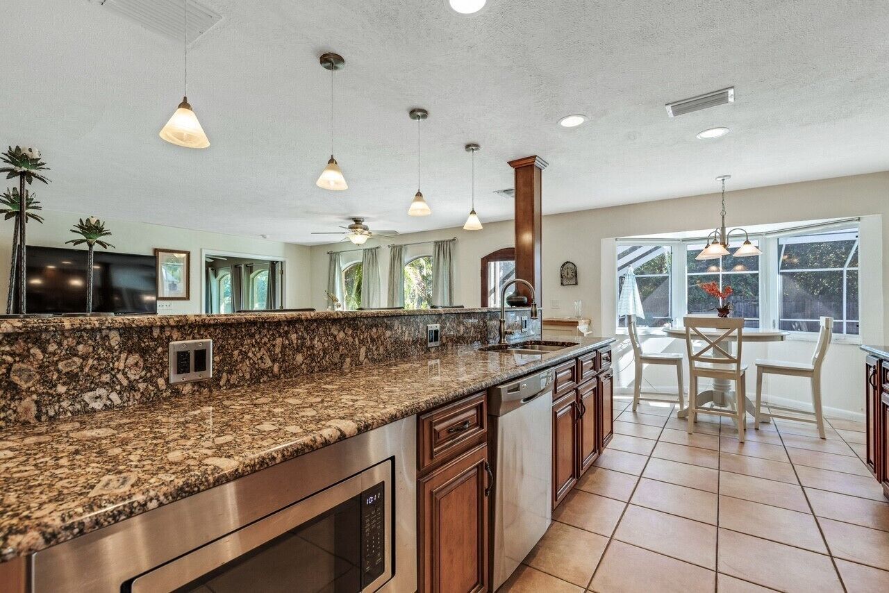 A spacious kitchen with granite countertops, stainless steel appliances, and wooden cabinets. There is a dining area with a table and chairs, and large windows providing natural light.