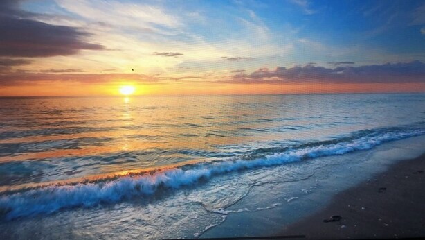 Eine Strandansicht mit untergehendem Sonnenuntergang über dem Meer, sanfte Wellen umspülen das Ufer.