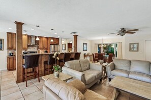 A spacious living area with a kitchen and dining area, featuring leather sofas, a bar, and wooden cabinets.