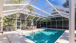 Ein überdachter Pool im Freien mit Glasverkleidung, umgeben von Bäumen und einem Holzzaun.