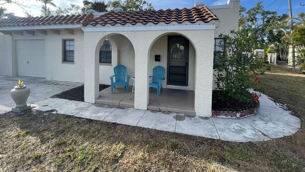 A single-story house with a tiled roof, two blue chairs, and a small porch. - The Historic McGregor Cottage (Fort Myers)