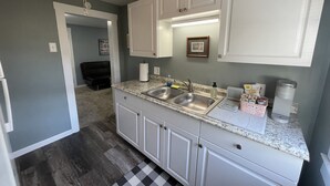 A compact kitchen with white cabinets, a double sink, and a ceiling fan. - The Historic McGregor Cottage (Fort Myers)