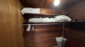 A small, wooden room with a bunk bed, a hanging towel rack, and a trash bin. - The Historic McGregor Cottage (Fort Myers)