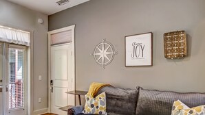 A living room with a grey sofa, patterned cushions, a compass wall decoration, and a framed motivational quote. - Charming Carriage House, Heated Pool Access (Savannah)