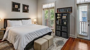 A bedroom with a bed, bedside tables, a bookshelf, and a window with blinds. - Charming Carriage House, Heated Pool Access (Savannah)