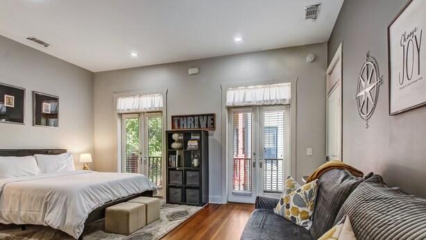 A bedroom with a bed, a sofa, a bookshelf, and a door with windows. - Charming Carriage House, Heated Pool Access (Savannah)