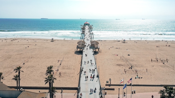 A beach with a long pier extending into the ocean, palm trees, and flags. - 30-Night Minimum Downtown HB - 1/2 mile to beach, Pier, Main St, & Pacific City (Huntington Beach)