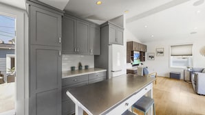 A modern kitchen with grey cabinets, a white refrigerator, and a dining area with a grey sofa and a small table. - 30-Night Minimum Downtown HB - 1/2 mile to beach, Pier, Main St, & Pacific City (Huntington Beach)