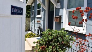 A house with an entrance sign, a window with a light fixture, and a bush with red flowers. - 30-Night Minimum Downtown HB - 1/2 mile to beach, Pier, Main St, & Pacific City (Huntington Beach)
