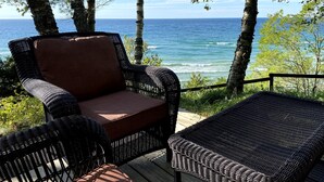 A wicker chair and a small table on a wooden deck overlooking the ocean. - NEW Scenic Lake Michigan House w/ Direct Access to Private Beach (Manistee)