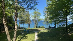 A pathway leading to a lakeside area with trees and outdoor seating. - NEW Scenic Lake Michigan House w/ Direct Access to Private Beach (Manistee)