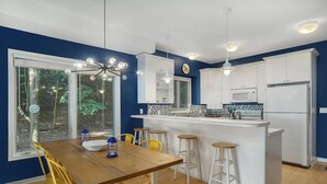A modern kitchen with white cabinets, a wooden dining table, and bar stools. - NEW Scenic Lake Michigan House w/ Direct Access to Private Beach (Manistee)