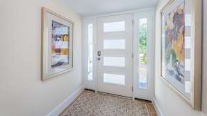 A hallway with a white door, a patterned rug, and two framed artworks on the walls. - Intercoastal waterfront home with Beautiful Bayside pool (Indian Rocks Beach)