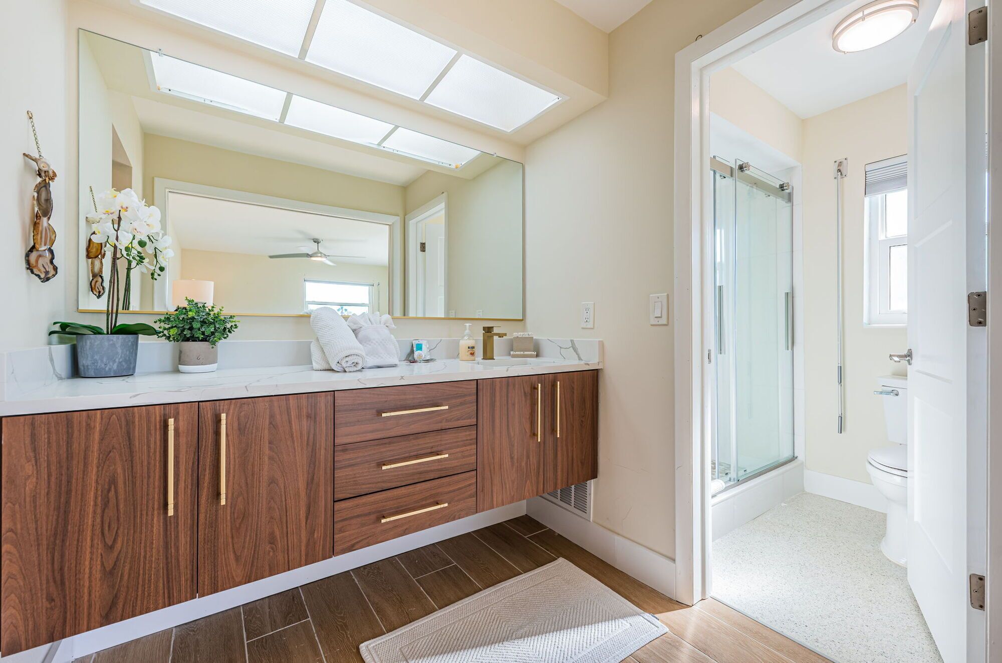 A modern bathroom with a large mirror, wooden vanity, and a shower area.