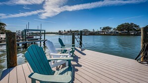 A wooden dock with chairs and tables, overlooking calm water with boats and houses in the background. - Intercoastal waterfront home with Beautiful Bayside pool (Indian Rocks Beach)