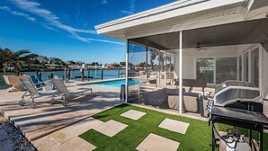 A modern outdoor pool area with lounge chairs, a grill, and a view of the marina. - Intercoastal waterfront home with Beautiful Bayside pool (Indian Rocks Beach)