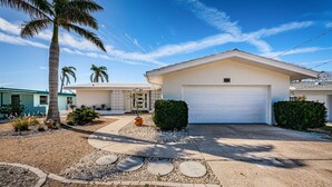 A single-story house with a white garage, a small front yard with palm trees, and a clear blue sky. - Intercoastal waterfront home with Beautiful Bayside pool (Indian Rocks Beach)