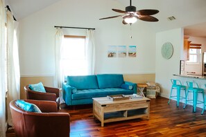 Ein Wohnzimmer mit einem blauen Sofa, zwei braunen Sesseln, einem Holztisch und einem Deckenventilator.