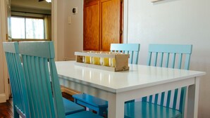 A dining area with a white table and blue chairs, a wooden door in the background, and a window with curtains. - Spacious and stylish 3bd home minutes from beach (Pass Christian)