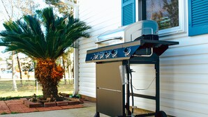 A portable grill with multiple burners and a storage compartment, positioned outside a house with blue shutters and a palm tree nearby. - Spacious and stylish 3bd home minutes from beach (Pass Christian)