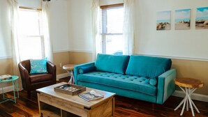 A living room with a teal sofa, a wooden coffee table, a brown leather armchair, and a small wooden side table. - Spacious and stylish 3bd home minutes from beach (Pass Christian)