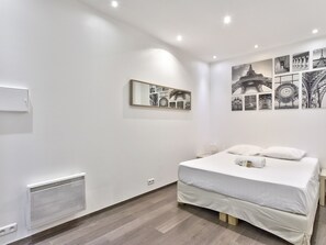 Une chambre moderne avec un grand lit, des murs blancs et des œuvres d’art représentant l’architecture parisienne.