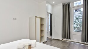 A modern hotel room with a bed, a wardrobe, and a view of the outside. - Appartement Ricca - Welkeys (Paris)