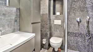 A modern bathroom with a large mirror, a white sink, a toilet, and a shower area with a glass door. - Appartement Ricca - Welkeys (Paris)