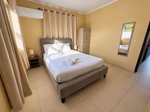 Un lit bien fait, avec du linge de lit et des serviettes blanches, une table de chevet avec une lampe, une armoire et un miroir au mur.