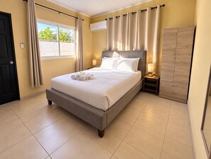 A bedroom with a bed, a wardrobe, a bedside table, and a window with curtains.