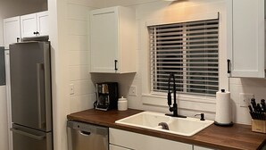 A modern kitchen with white cabinets, a stainless steel refrigerator, a wooden countertop, a sink, and a window with blinds.