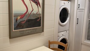 A room with a framed poster of a flamingo, a washing machine, and a table with chairs.