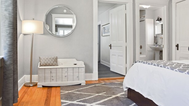 A bedroom with a bed, a dresser, a mirror, a floor lamp, and a bathroom visible through an open door. - Ivywild Bungalow ↠Close to Trails/Downtown/Shops↞ (Colorado Springs)