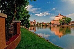 Overlooking a serene lake, this building features a tower and multiple windows surrounded by lush greenery and calm waters.