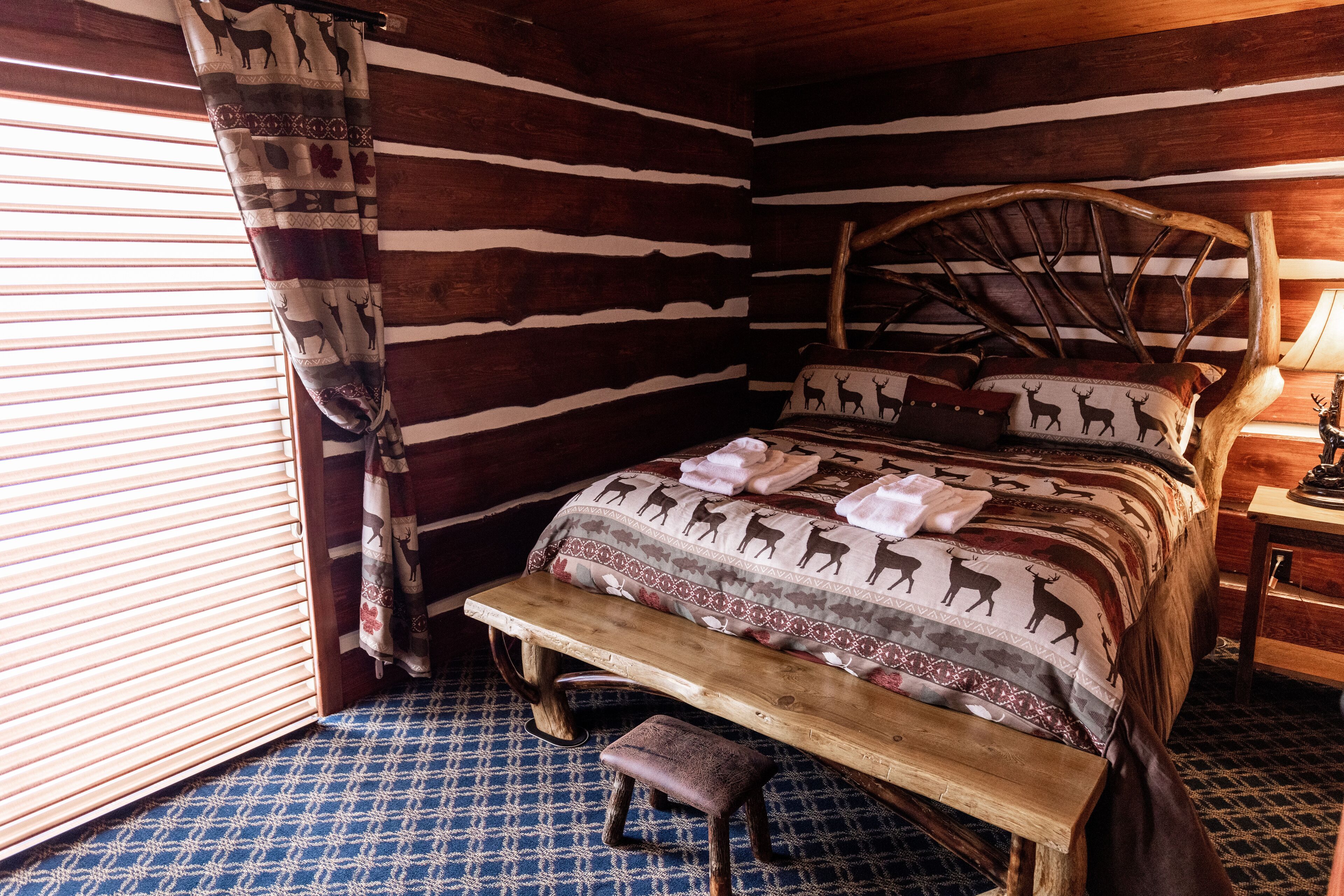 Une chambre rustique avec un lit orné de motifs animaliers, un banc en bois et une fenêtre avec des stores.