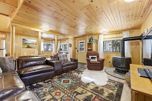 L’intérieur d’un chalet accueillant, avec un canapé en cuir, un fauteuil moelleux, un tapis et un poêle à bois.