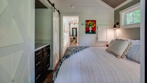 Un dormitorio con una cama grande, un aparador, un cuadro de flores y una ventana con vistas.
