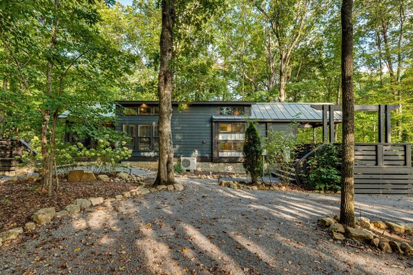 Een modern huis met een grindpad, omringd door bomen en een houten hek.