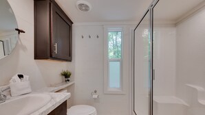 Un baño con un lavabo blanco, muebles de madera oscura, un inodoro y una cabina de ducha de vidrio.