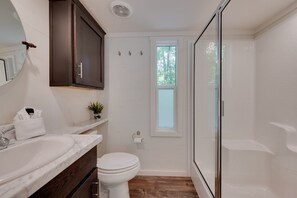 Une salle de bain avec un lavabo blanc, des meubles en bois foncé, des toilettes et une douche à parois de verre.