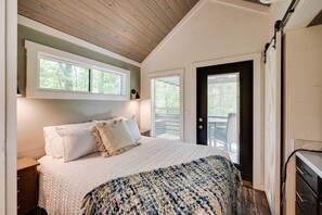 Een slaapkamer met een groot bed, een houten plafond en een deur naar een balkon.
