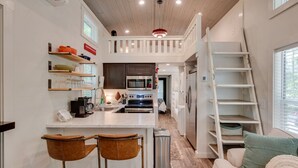Una cocina compacta con una isla central, un comedor con dos taburetes y un espacio para dormir elevado con escalera.