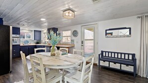 A dining area with a round table, white chairs, a bench, and a decorative vase.