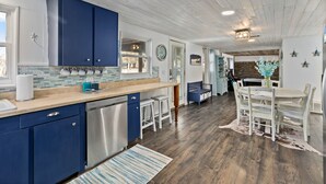 A kitchen with blue cabinets, a dishwasher, and a dining area with a table and chairs.