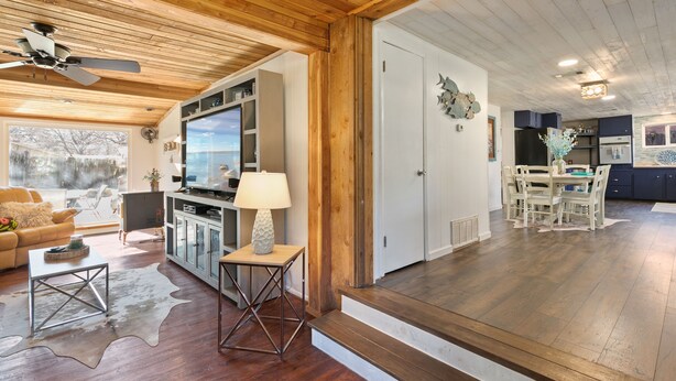 A spacious living area with wooden flooring, a ceiling fan, a TV, and a dining area with a table and chairs.