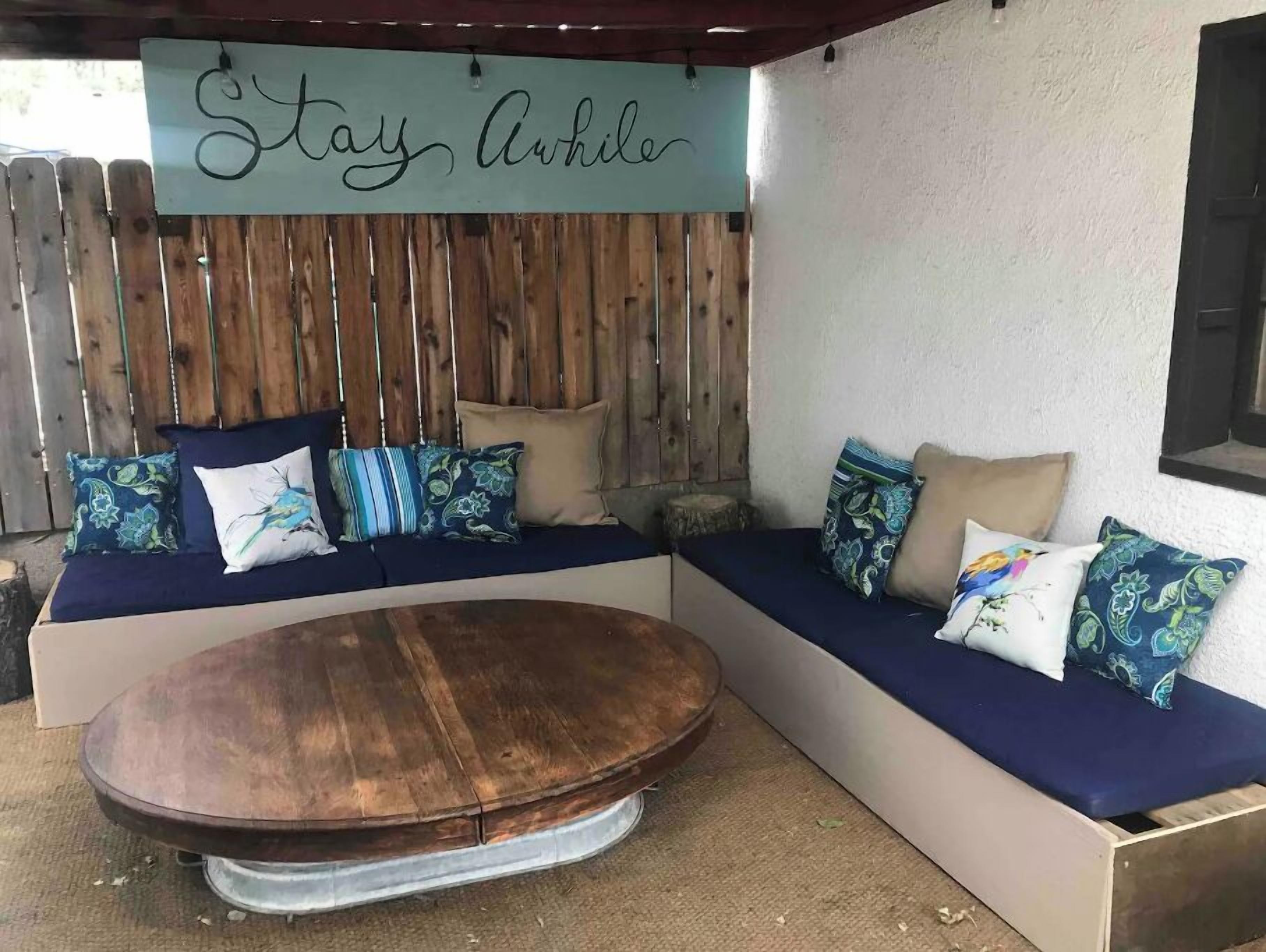 Un espacio al aire libre acogedor con un banco de madera y asientos acolchados, una cerca de madera y un letrero que dice 