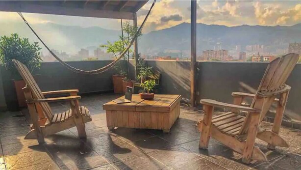 A wooden deck with two chairs and a table, a hammock, and potted plants. - Airy Penthouse with Private Rooftop Terrace in a Quaint Colombian Neighbourhood (Envigado)