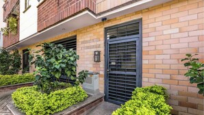 A building with a brick facade, a black metal gate, and green shrubs in front. - Airy Penthouse with Private Rooftop Terrace in a Quaint Colombian Neighbourhood (Envigado)